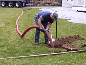 Septic pumping technician servicing a residential septic tank with a vacuum hose in Troy, MI