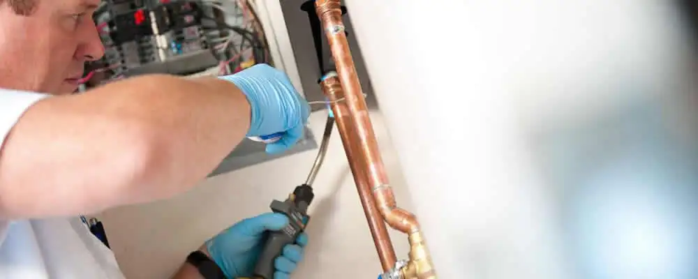 Water heater repair technician testing copper pipe connections and controls in Troy, MI